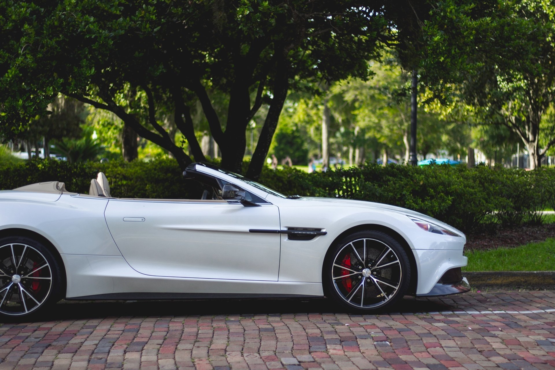 White convertible parked on brick road with green trees in background.